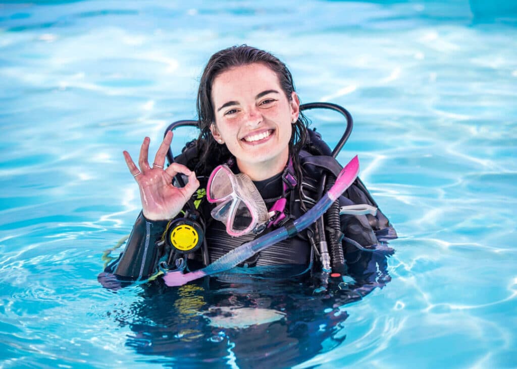 Girl holding up OK sign in swimming pool preparing for diving course