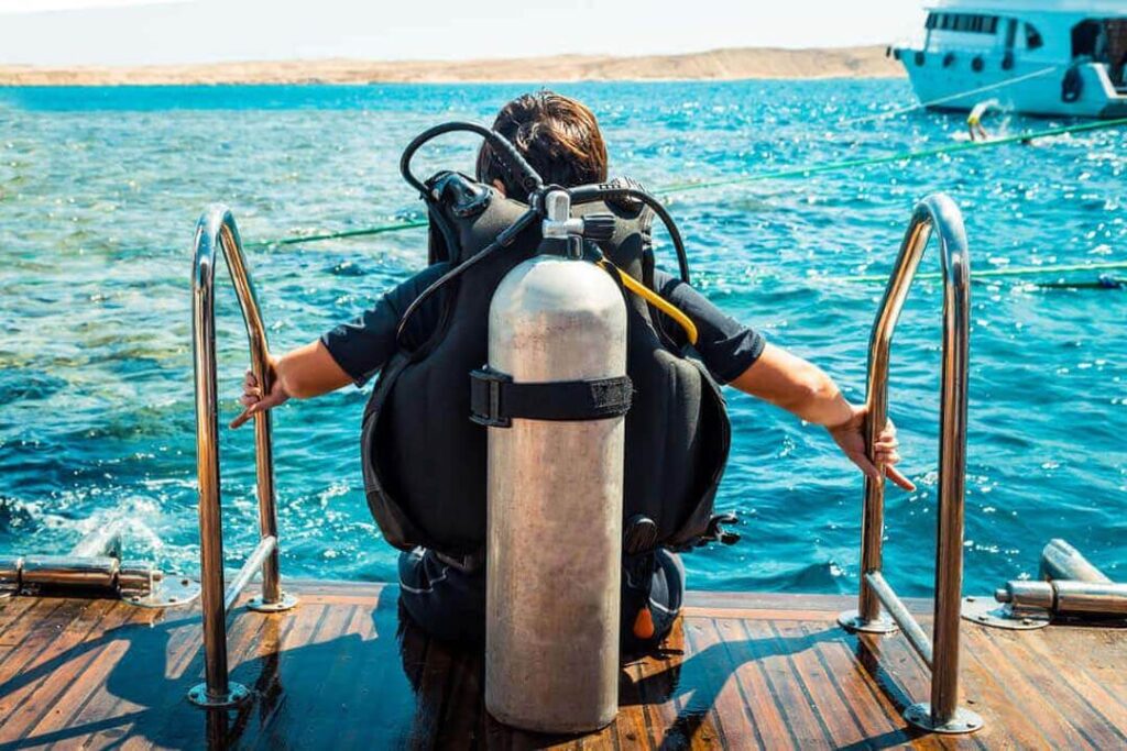 A woman equipped with a scuba tank prepares to dive from the deck of a boat, excited to explore the Red Sea in Hurghada.