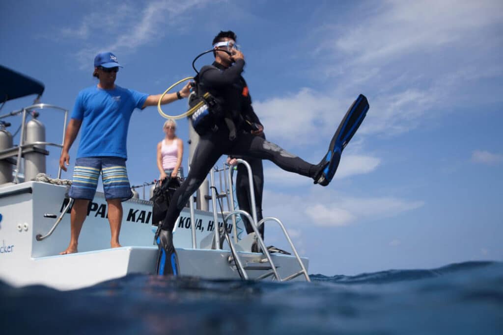 man helps diver jump from boat