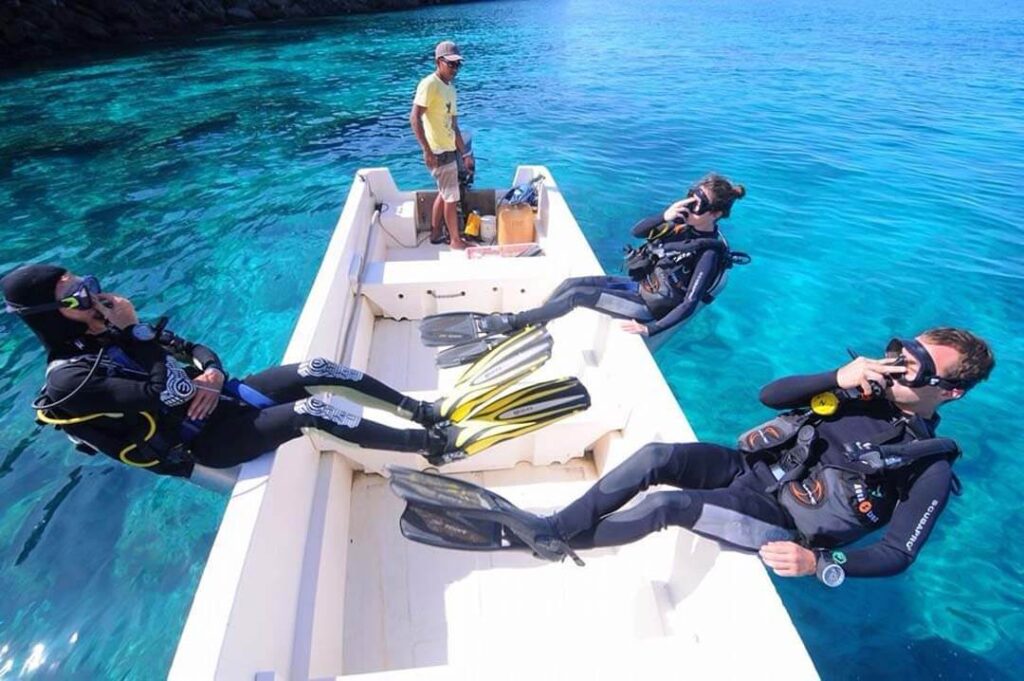 Three scuba divers wearing gear, swimming in clear water, ready to discover marine life beneath the surface.