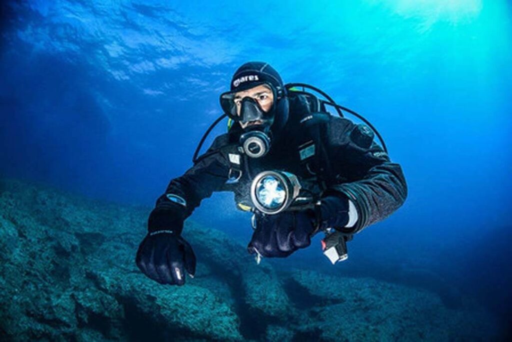 A scuba diver exploring underwater with a flashlight, illuminating the depths around them.