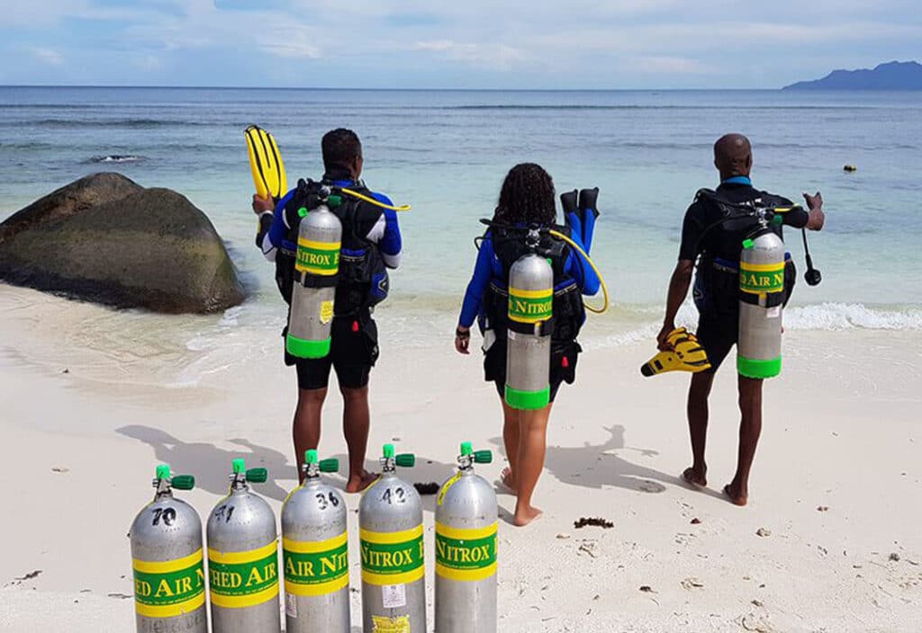 Two men and a woman on the beach going to scuba dive using nitrox tanks.