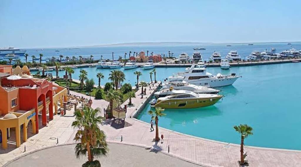 Scenic view of Hurghada Marina with luxury boats and yachts, colorful buildings lining the promenade, and the tranquil waters of the Red Sea.