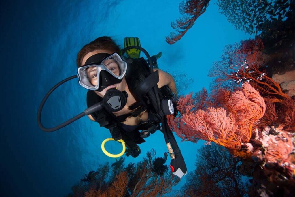 A woman scuba diver wearing a mask and snorkel, exploring underwater in clear blue water.