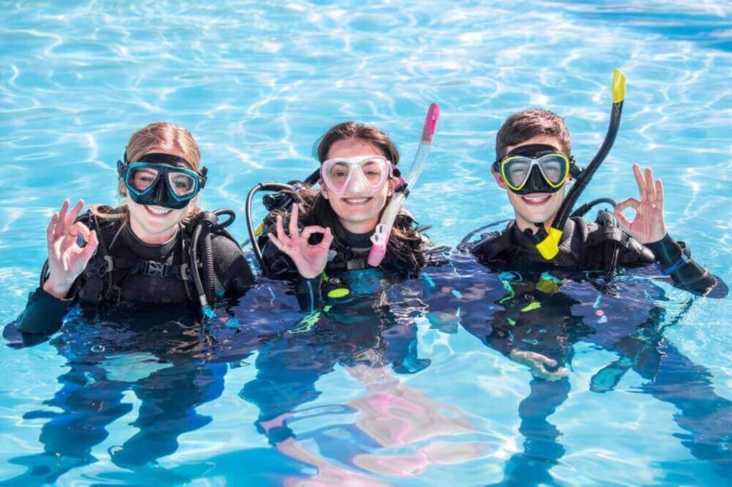 Three individuals in scuba gear smiling and posing for a photo in a clear blue swimming pool.