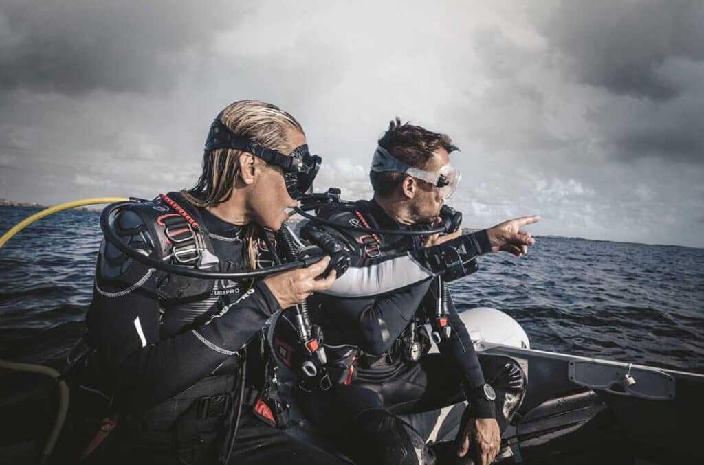 Two scuba divers on a boat, indicating an object of interest as they prepare for their underwater exploration.