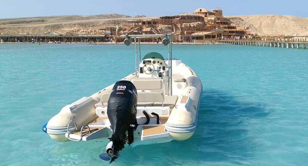 A motorboat gliding on the water near the sandy shores of Orange Bay Island in Hurghada, with sunlight shimmering on the Red Sea waves.