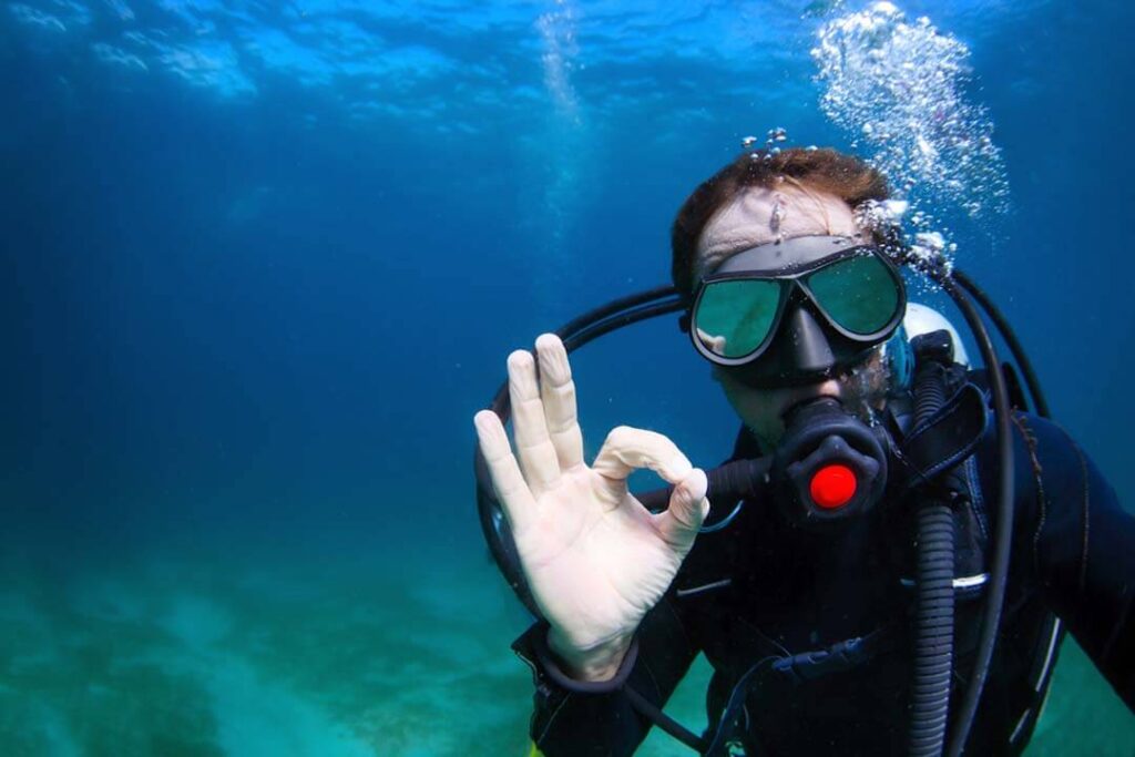 A scuba diver in the ocean raises his hand, indicating a gesture while exploring the underwater environment.