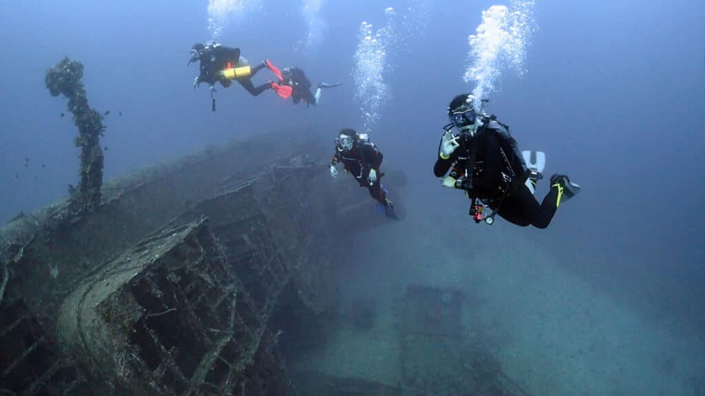 Four divers near a shipwreck.