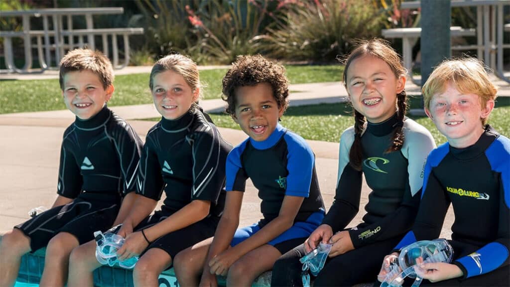 Five young children sitting in a pool preparing for the PADI Bubblemaker Course.