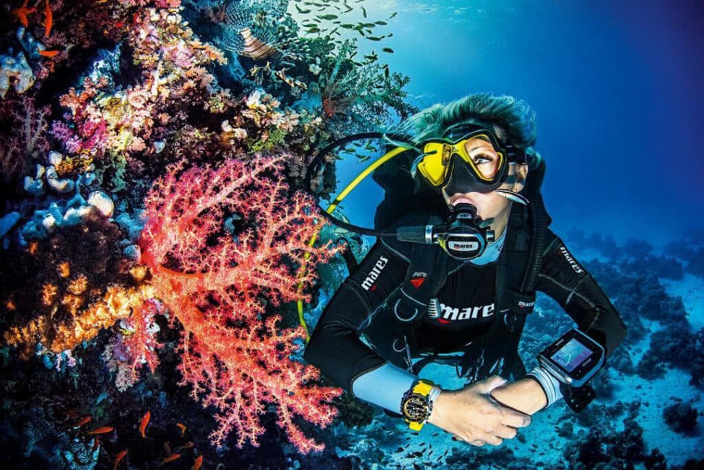 A scuba diver explores vibrant coral reefs, surrounded by colorful fish in clear blue water. Dive-forever | diving center in hurghada