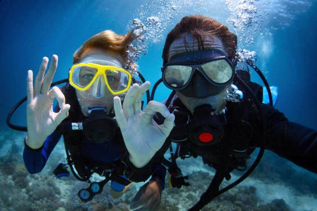 Photo of two divers underwater raising the OK sign with their hands while diving